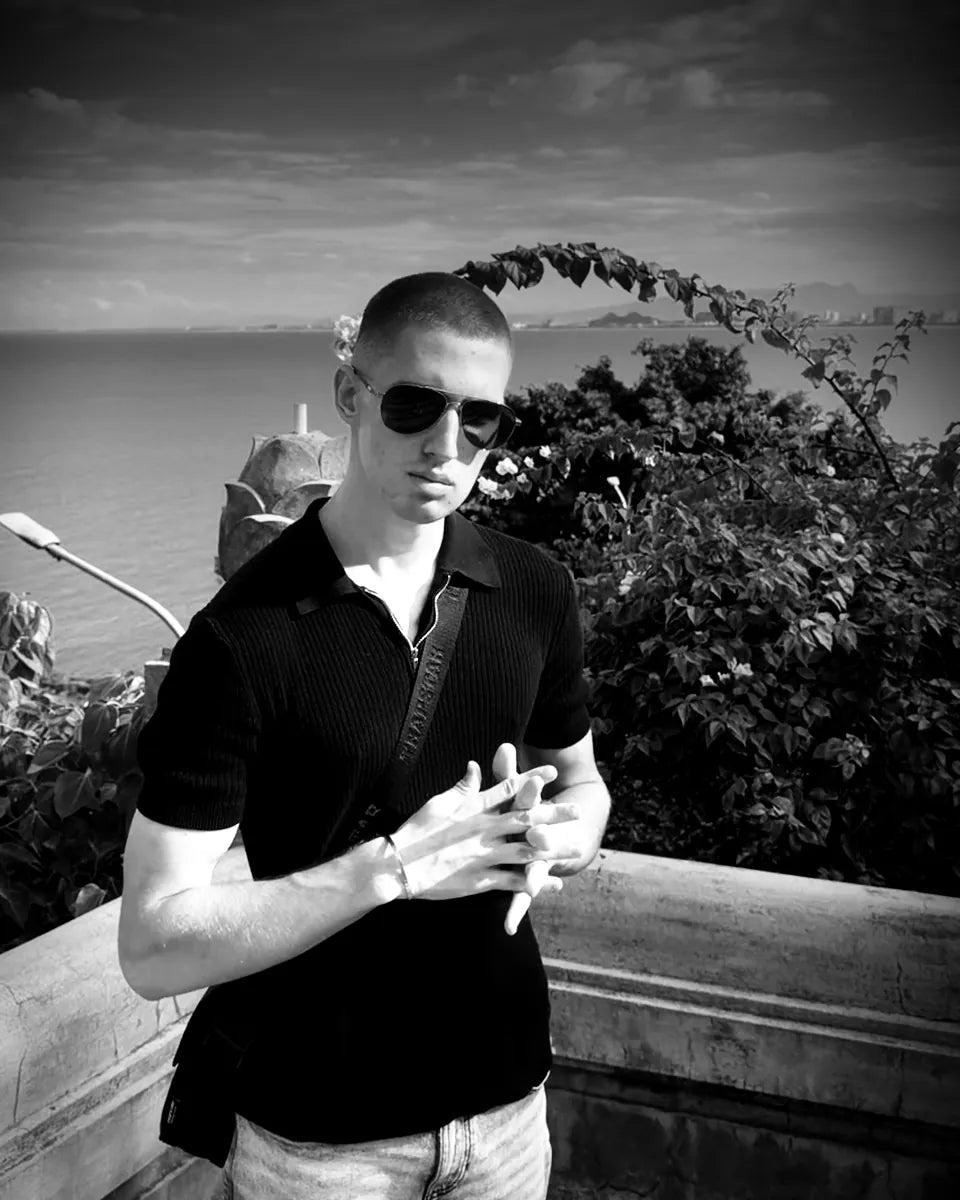 WristyBoi in sunglasses, hands together, the sea behind him